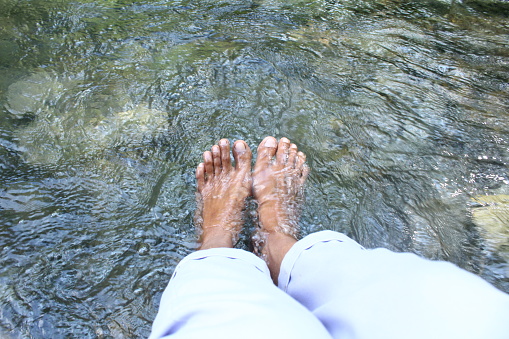 Asian woman soaking her feet in water to feel fresh and relaxed. Enjoy nature with trees, rivers, mountains and fresh air