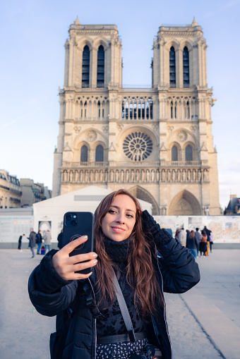 Positive Latina woman tourist smiling and taking selfie in Notre Dame cathedral, Paris France