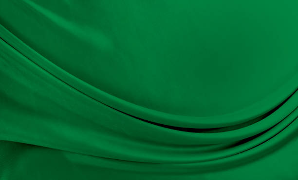 Black green satin dark fabric texture luxurious shiny that is abstract silk cloth background with patterns soft waves blur beautiful.