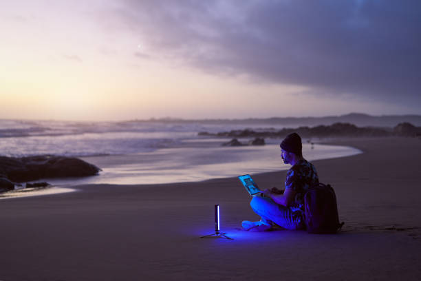 side view silhouette mature digital nomad man sitting on the beach shore working on his laptop at sunset