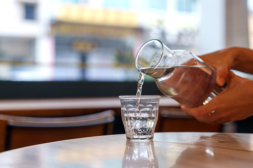 Cropped shot of a woman pouring water from a bottle into a glass in a cafe