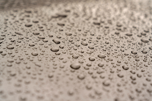 A full frame capturing the textures formed by drops of water on a gray metal background