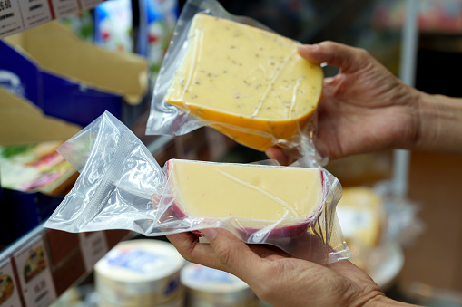 An Asian woman grocery shopping in a supermarket, carefully selecting fresh packets of cheese from the dairy aisle. She is focused on eating well and maintaining a balanced nutrition.