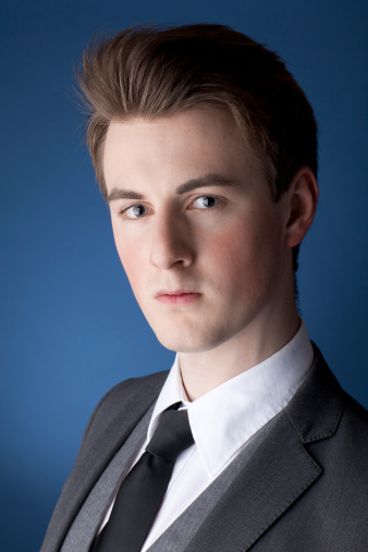 A portrait of a handsome, young man, wearing a suit, against a blue background.