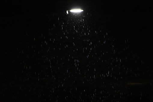 Raindrops and a streetlight at dark night time .