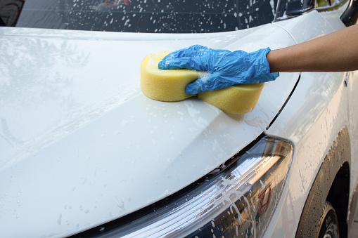 Worker hand using sponge with soap to wash white car. Car care concept.