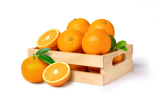 Orange fruit with half slice and green leaves in wooden box isolated on white background.
