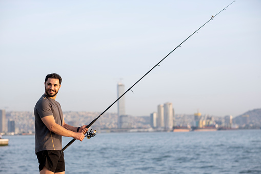 Handsome young man fishing in his spare time in the city.
He spends time by the sea to relax.