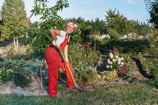 A happy female gardener in gloves and an apron stands against in a home garden . Gardening and floriculture. Flower care.