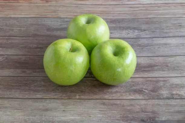 An overhead view of four ripe apples placed on a wooden board