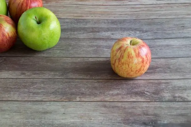 Three red apples are displayed side-by-side on a wooden floor in an attractive arrangement