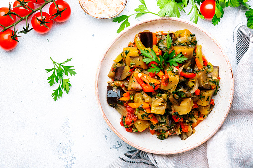 Vegetable stew, saute or caponata. Stewed eggplant with red paprika, tomatoes, garlic, onion, spices and herbs. White kitchen table background, top view