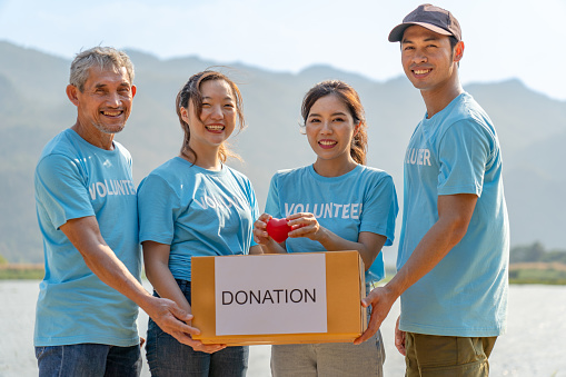 group of diverse volunteers carrying donation box and a red heart charitable join working together raising money campaign to help underprivileged people by donate food, clothing or support education