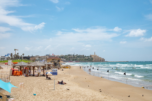 Tel Aviv, Israel - May 18, 2023: people enjoy the beautiful sandy beach in Tel Aviv on a summer day. In the background the old town of Tel Aviv.