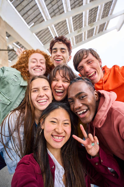 Vertical multi-ethnic group smiling student boys and girls taking selfie outdoors. People enjoying.