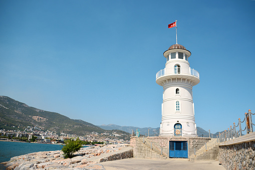 A lighthouse on the coast of the city with mountains on background, copy space