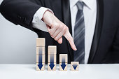 Wooden blocks with dark blue arrows icons, businessman in suit pointing down against white background, business decline loss drop concept