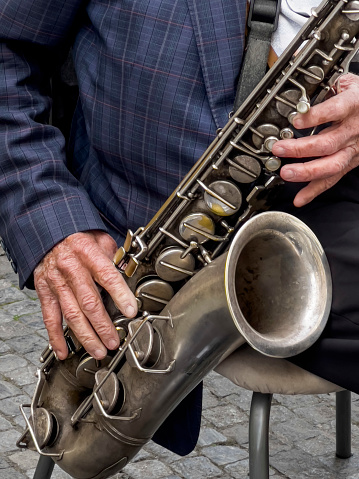 saxophone, closeup wrinkled hands of an old man or male musician playing the saxophone. street musician performing a musical instrument. performing street art