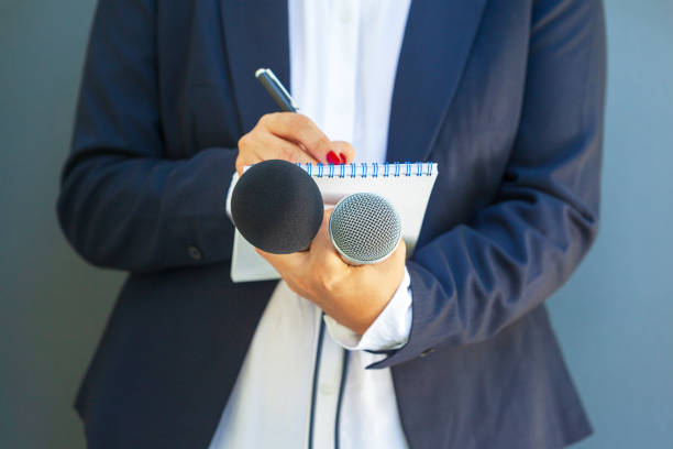 Journalist at media event or news conference, holding microphone, writing notes. Broadcast journalism concept. stock photo