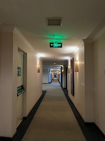 The photograph highlights a crucial element of safety and preparedness—a vibrant green emergency exit sign positioned in a hotel corridor. This sign, prominently displaying the word \