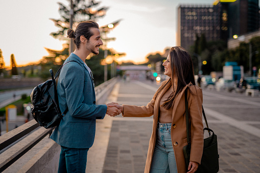 Businessman and businesswoman meeting in city, shaking hands and smiling on sidewalk