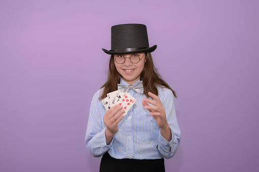 Beginning novice magician conjurer. Girl with cards in her hands in a hat with a top hat and a striped shirt with a bow tie