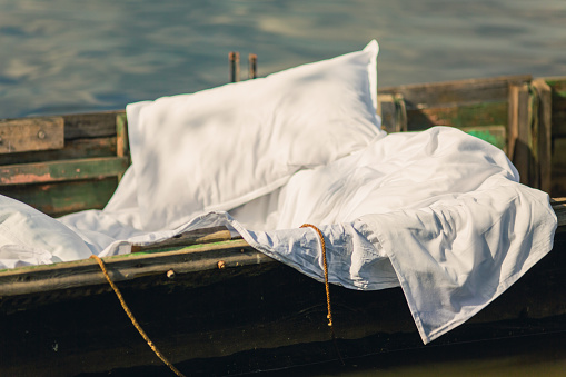 White linens in old fishing boat. Lake. Bed sheets
