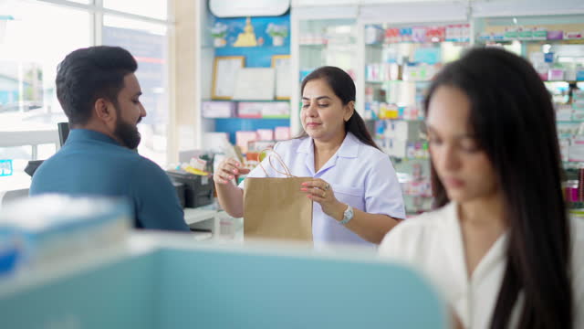4K Indian woman pharmacist selling medicine and supplements to male customer at drugstore.
