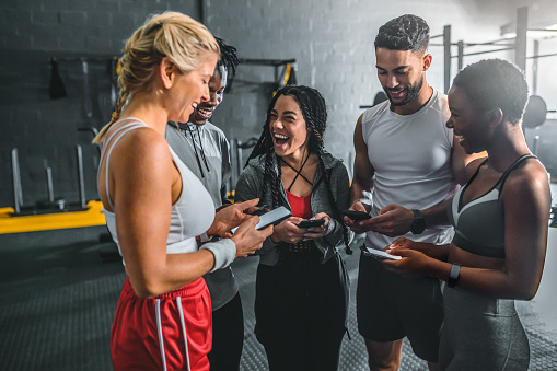 Excited woman and friends streaming on social media with cellphone, laughing and sharing stories in gym