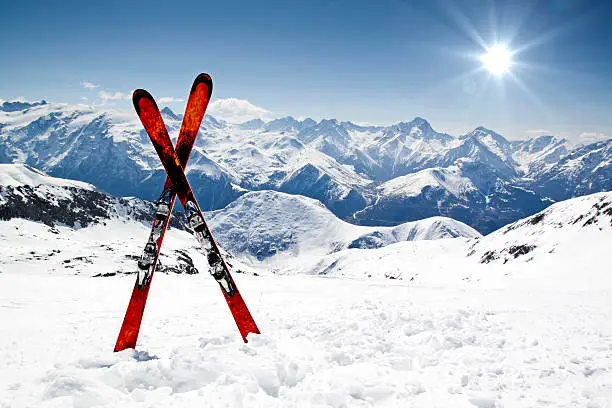 Photo of Pair of red skis crossed and wedged in snow on mountain