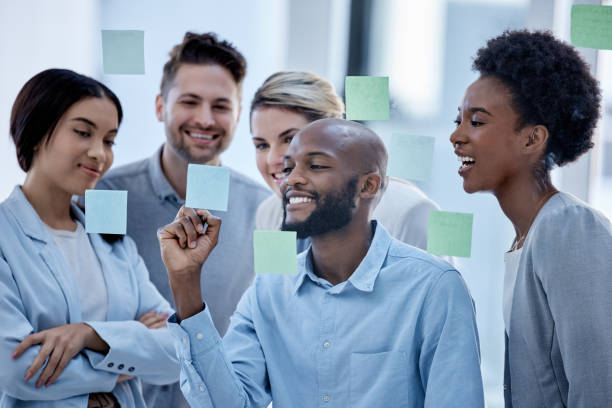 istock Business, team and black man writing on sticky note, brainstorming and planning for project, smile and collaboration. Corporate, Nigerian male leader or staff share ideas, advertising agency or sales 1493963890