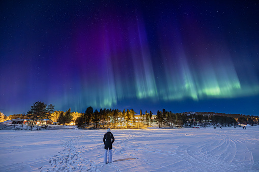 Young girl watching purple, blue and green Northern lights (aurora borealis) 
above Ounasjärvi lake in Hetta, Lapland, Finland