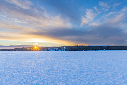 Scenic Winter Landscape. Frozen snow-covered arctic lake surrounded with forest trees  at the waterfront under sunny clear sky. Edited Colors. Finnish Lapland in Winter. Ivalo, Finland, Scandinavian Countries, Northern Europe.