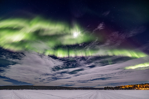 Green Northern lights (aurora borealis)  with moon\nabove Ounasjärvi lake in Hetta, Lapland, Finland
