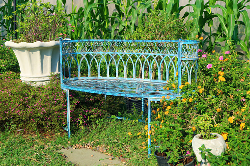 Empty vintage blue colored wrought iron bench in the garden