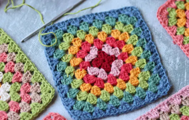Colorful crochet Granny squares on light grey background with copy space. Handmade blanket in process. Multicolored vintage ornament. Hippie fashion concept.