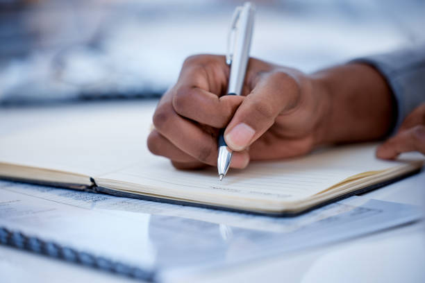 istock Business, black man and hands writing in notebook, diary and strategy ideas. Closeup worker planning with pen, notes and schedule of information in journal, reports or logistics agenda at office desk 1493974153