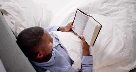 Happy Young African Man Reading His Book On Bed