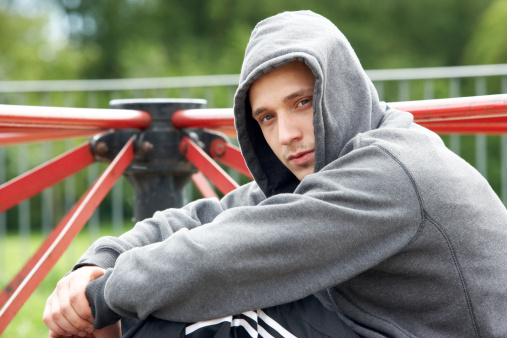 Young Man Wearing Hoodie Sitting in In Playground