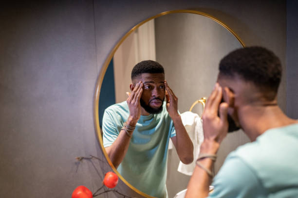 homem afro-americano preocupado olha para o espelho, toca a pele do rosto ansioso por rugas. - mirror men depression african descent - fotografias e filmes do acervo