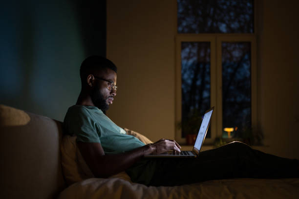 istock Concentrated African American programmer man lying on bed work on laptop at night. 1493987898
