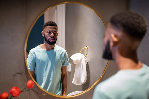 homem afro-americano infeliz se olhando no espelho no banheiro, sentindo-se insatisfeito com sua aparência - mirror men depression african descent - fotografias e filmes do acervo