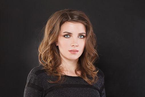 Portrait of nice elegant woman with brown wavy hair and makeup on black background