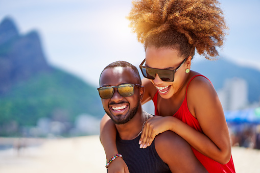 head shot portrait young black brazilian couple in piggyback position having fun in Ipanema beach Brazil