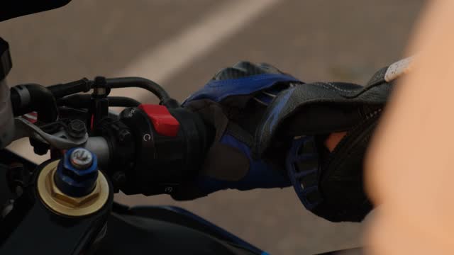 A biker's hand in a leather glove takes the wheel of a motorcycle. Close-up.