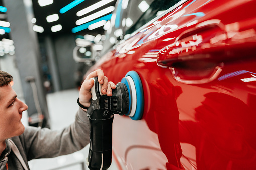 Professional vehicle polishing and detailing service in a modern car workshop. Brightly lit workspace with large led lights. High quality car valeting concept.