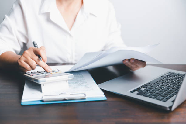 istock Close up woman with calculator counting making notes at home, hand is writing in a notebook. Asian woman checking bills, taxes, bank account balance and calculating credit card expenses. 1494021050