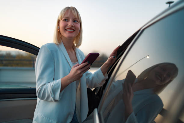 istock Woman using her smart phone while standing near modern car outdoors 1494021190