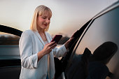 A business woman uses a smartphone while leaning on her premium car.