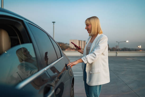 istock Woman using her smart phone while standing near modern car outdoors 1494021213